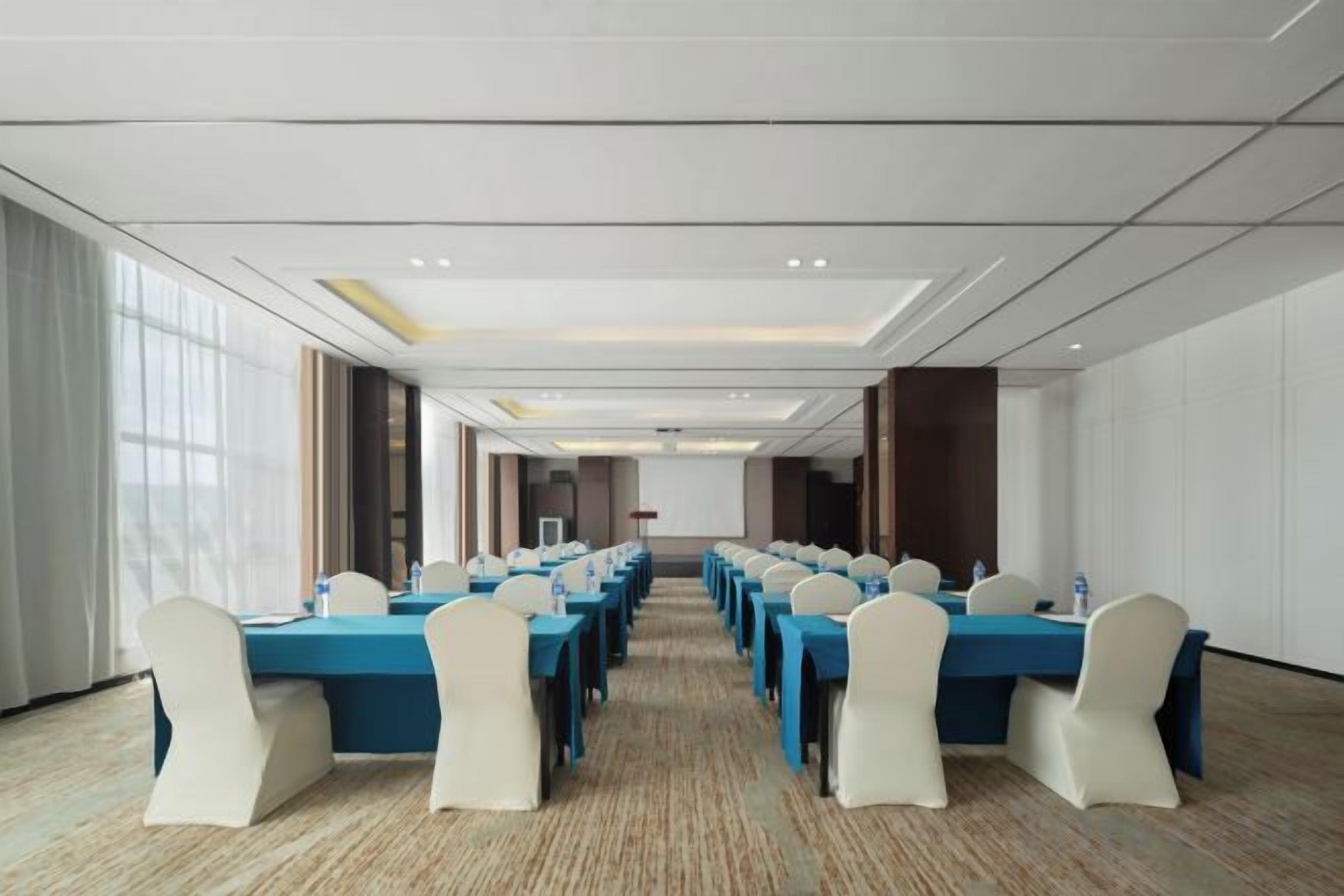 A conference room with long tables and chairs, large windows, and a carpeted floor.