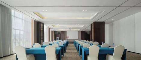 A conference room with long tables and chairs, large windows, and a carpeted floor.