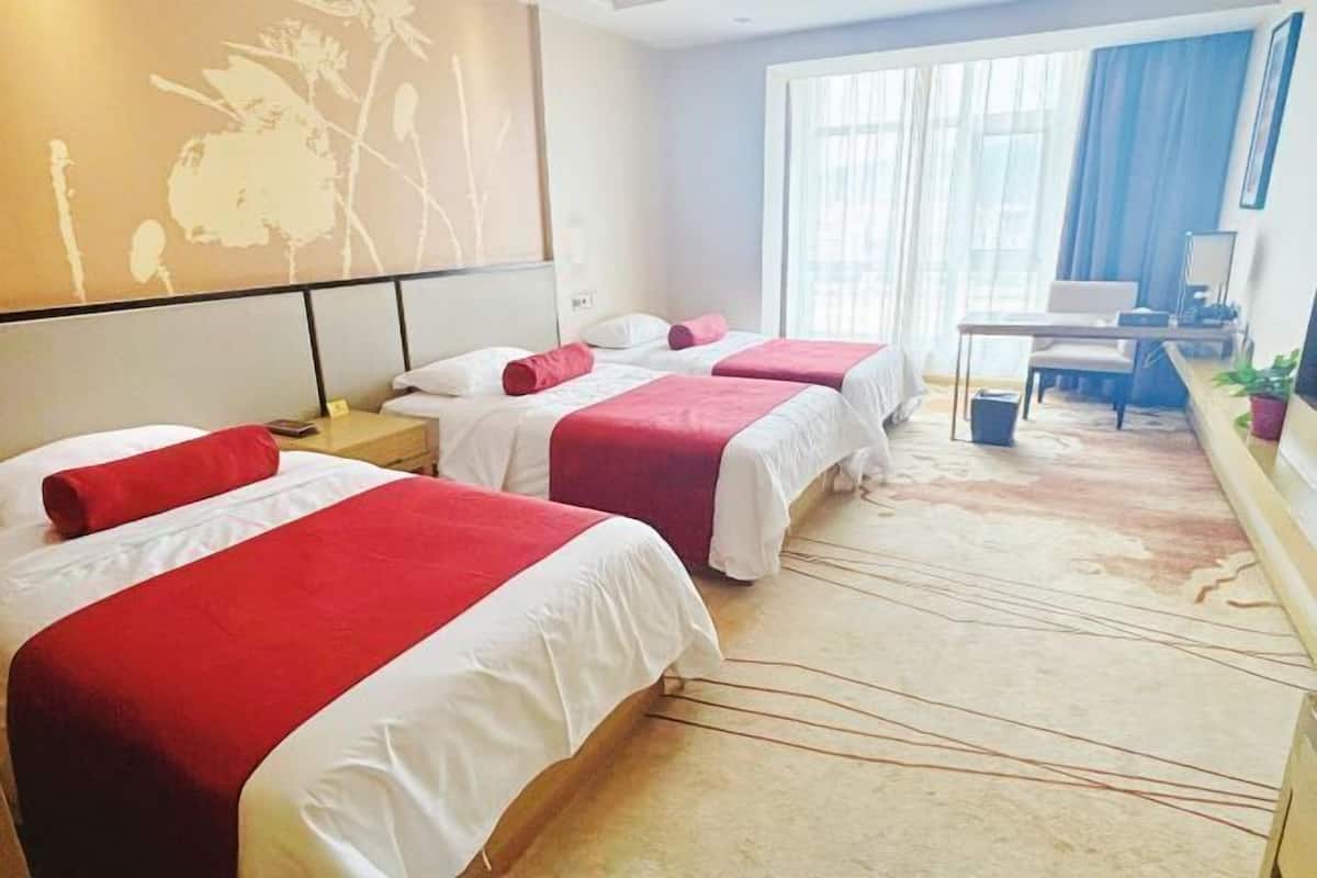 Habitación de hotel con dos camas, un escritorio, una silla y un ventanal con cortinas.