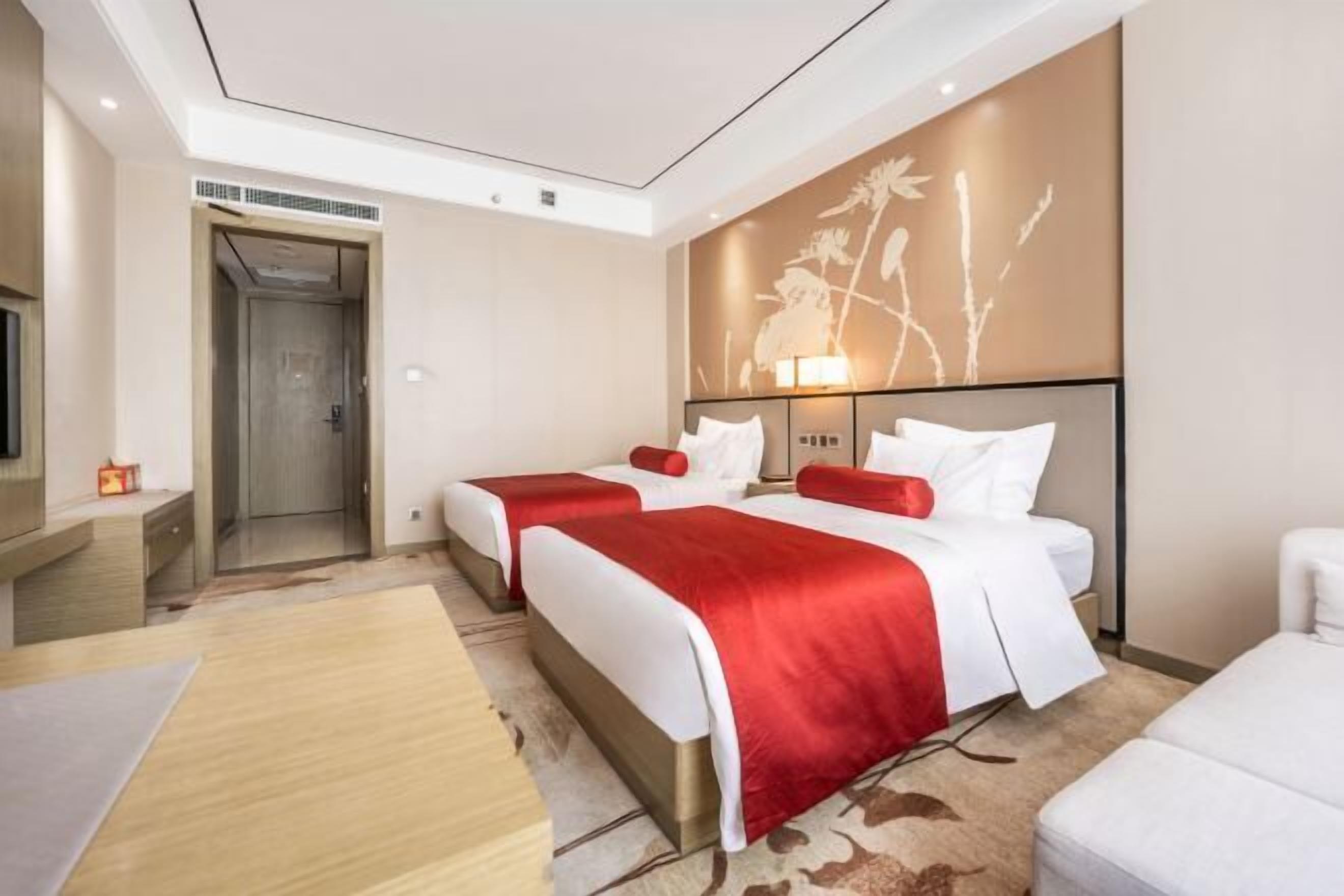 A hotel room with two beds, a wooden floor, a large wall mural, and a television on a stand.
