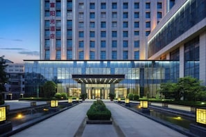 A modern hotel with a glass facade, a central entrance, and a well-lit outdoor area with water features. - Fortune Sunshine Hotel (Tianshui)