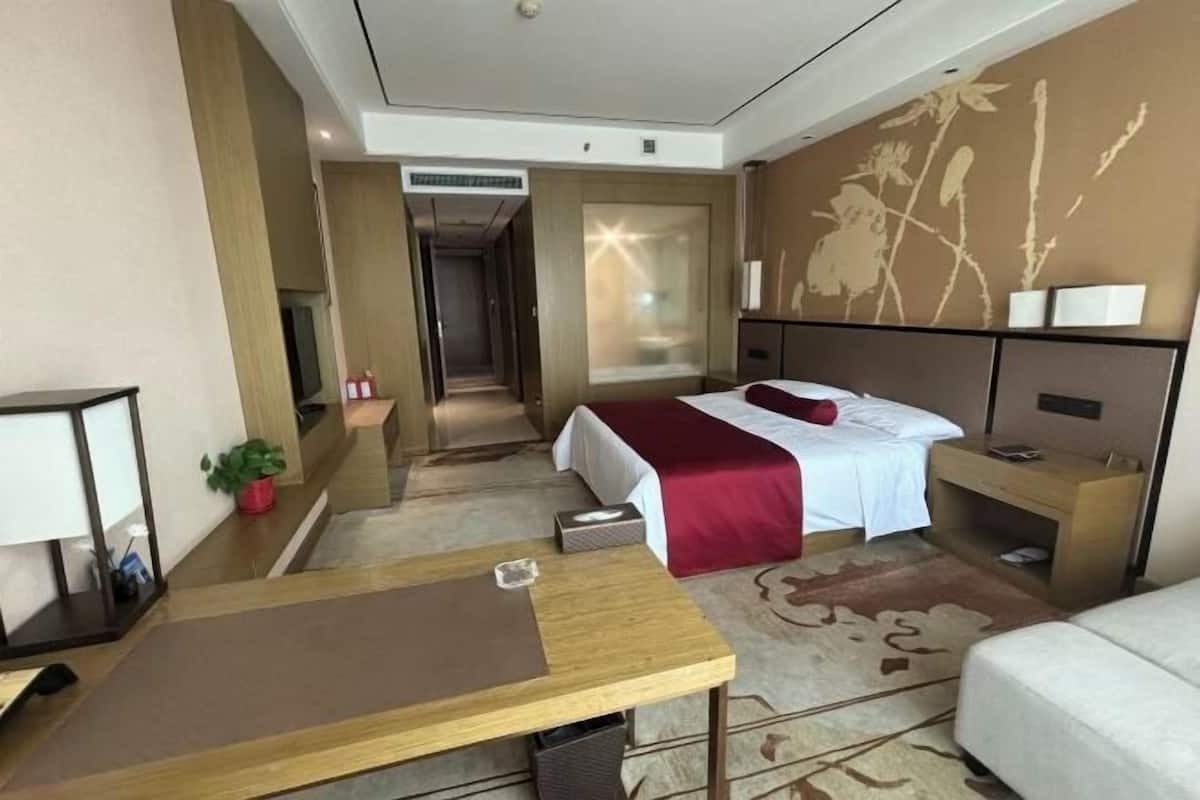 Habitación de hotel con cama, mesita de noche, escritorio y vista al pasillo.