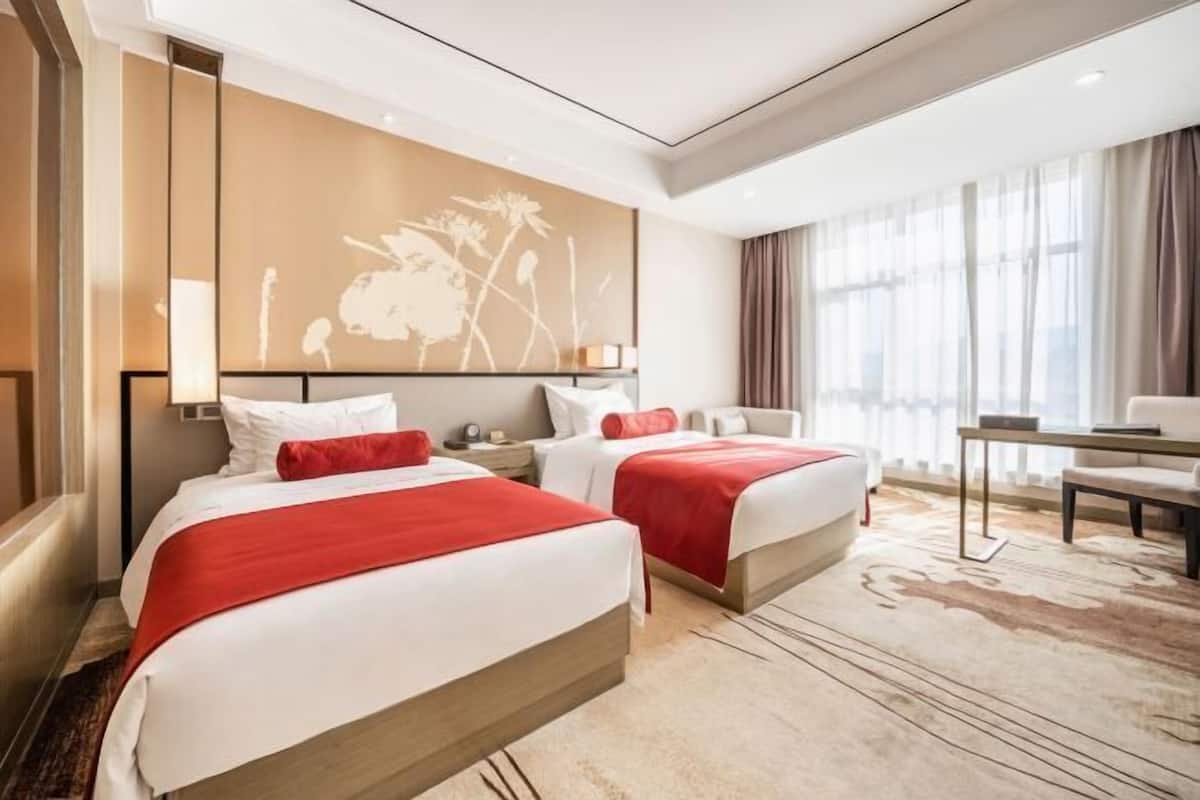 Habitación de hotel con dos camas, un ventanal con cortinas, un escritorio y una obra de arte en la pared.