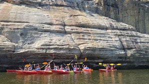 A group of people kayaking in red kayaks with a rocky cliff in the background.