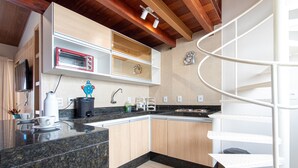 Una cocina moderna con horno empotrado, microondas y cafetera. Hay una encimera de madera y una escalera de caracol al fondo.