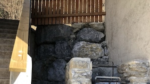 A stone-built outdoor fireplace with a metal grate, surrounded by logs.