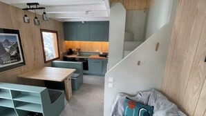 A compact kitchen with teal cabinets, a wooden countertop, and a dining area with a bench and shelves.