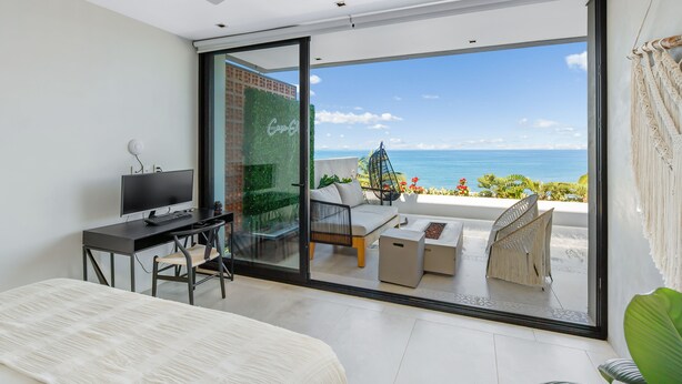 Ein modernes Schlafzimmer mit einer großen Schiebeglasdoor zum Balkon mit Meerblick.
