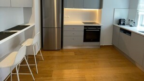 A modern kitchen with a built-in refrigerator, oven, and dishwasher. There are white chairs and a small dining table. - Athens Riviera 2-Bed Apt & Pool Access #Unoblu® (Alimos)
