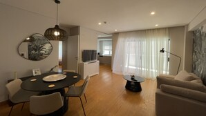 A modern living room with a round dining table, a sofa, and a TV in the background. - Athens Riviera 2-Bed Apt & Pool Access #Unoblu® (Alimos)