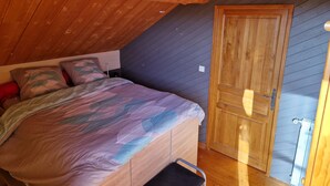 Un dormitorio con techo de madera, cama con ropa de cama estampada, una mesita de noche y una puerta de madera.