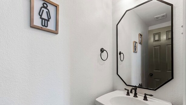 A bathroom with a white sink, a large mirror, and a framed female restroom symbol. - 5BR Bonnie Home Steps from It All! (Austin)
