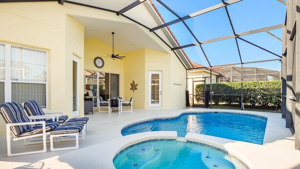 An indoor swimming pool with lounge chairs, a ceiling fan, and a glass enclosure. - Modern 5 bed villa on gated community, 20 minutes from Disney (Davenport)