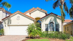 A two-story house with a white garage door, a small porch with a window, and a palm tree in the front yard. - Modern 5 bed villa on gated community, 20 minutes from Disney (Davenport)