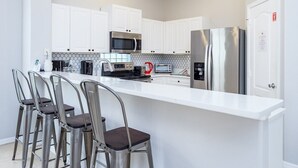 A modern kitchen with white cabinets, stainless steel appliances, and a central island with bar stools. - Modern 5 bed villa on gated community, 20 minutes from Disney (Davenport)