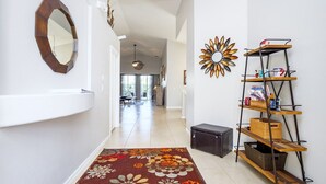 A hallway with a floral rug, a mirror, a sun-shaped wall decoration, and a metal shelf unit. - Modern 5 bed villa on gated community, 20 minutes from Disney (Davenport)