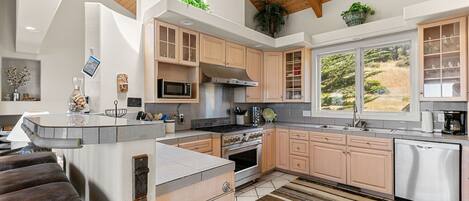 A modern kitchen with wooden cabinets, stainless steel appliances, a large window, and a built-in island.