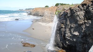 A coastal scene with a rocky cliff, a waterfall, and a sandy beach. - Stunning views near beaches and bluff (Sea Ranch)