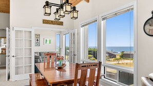 A dining area with a wooden table, chairs, and a chandelier. There is a large window with a view of the ocean and a sign above the window that reads "Pacific Pear - The Sea Ranch, CA." - Stunning views near beaches and bluff (Sea Ranch)