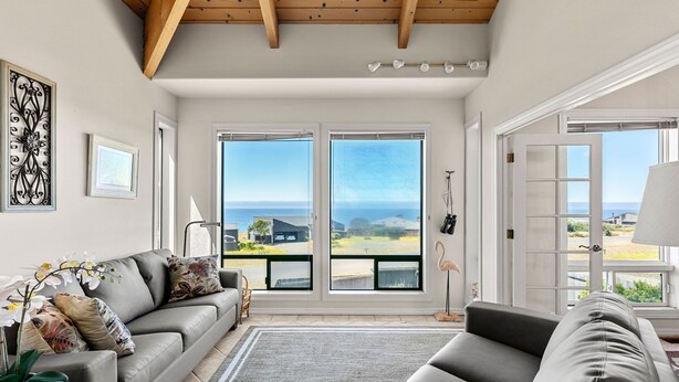 A spacious living room with a grey sofa, a coffee table, and a view of the ocean through large sliding glass doors. - Stunning views near beaches and bluff (Sea Ranch)