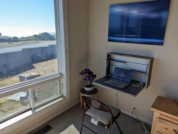 A room with a desk, a laptop, a chair, a TV mounted on the wall, and a window with a view of a parking lot. - Stunning views near beaches and bluff (Sea Ranch)