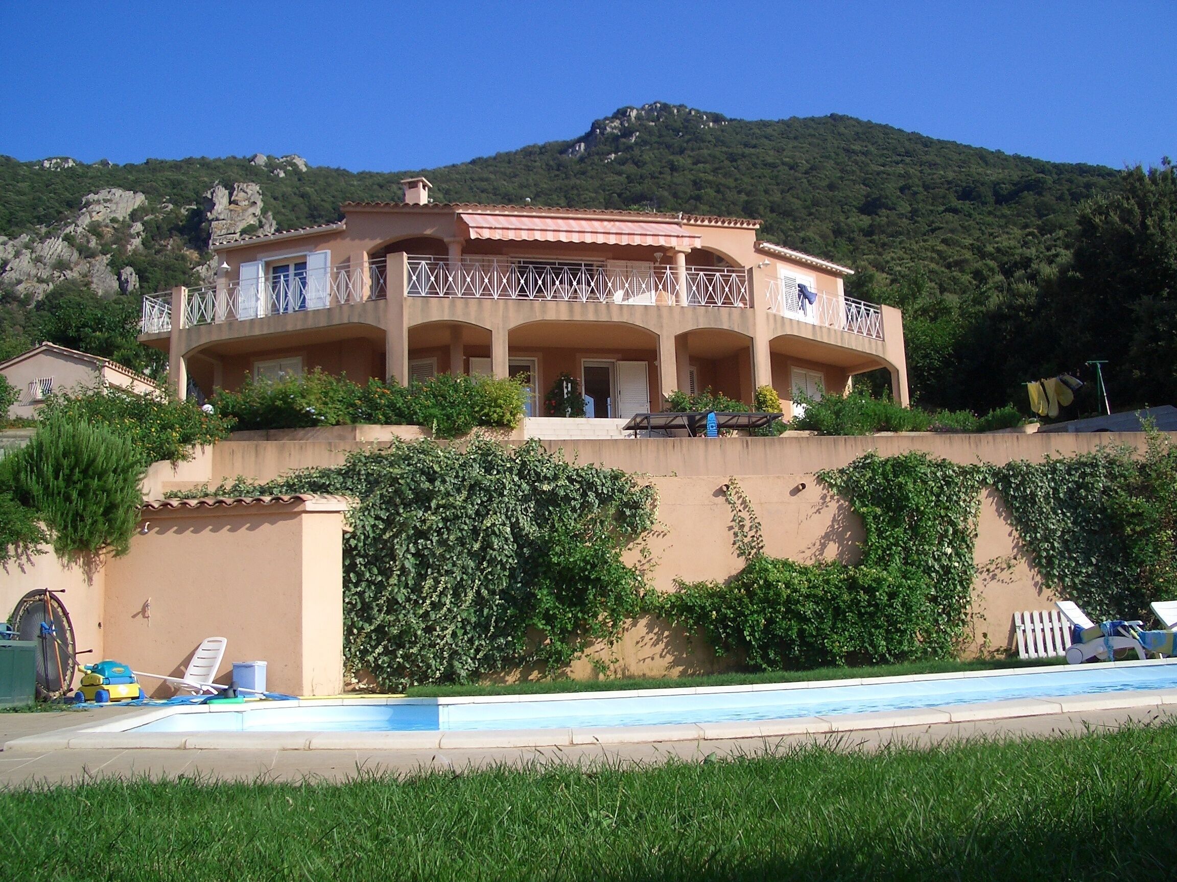 A multi-story building with balconies, a swimming pool, and a mountainous backdrop.