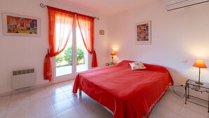 Um quarto com uma cama grande, duas luminárias de cabeceira, uma janela com cortinas vermelhas e duas fotos emolduradas nas paredes.