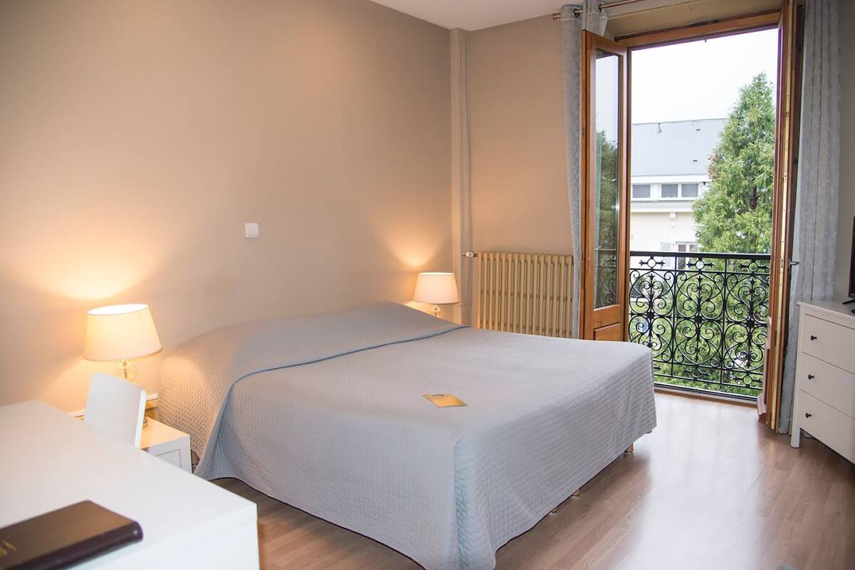 Habitación de hotel con cama, lámparas de noche, escritorio y vistas a un balcón con barandilla.