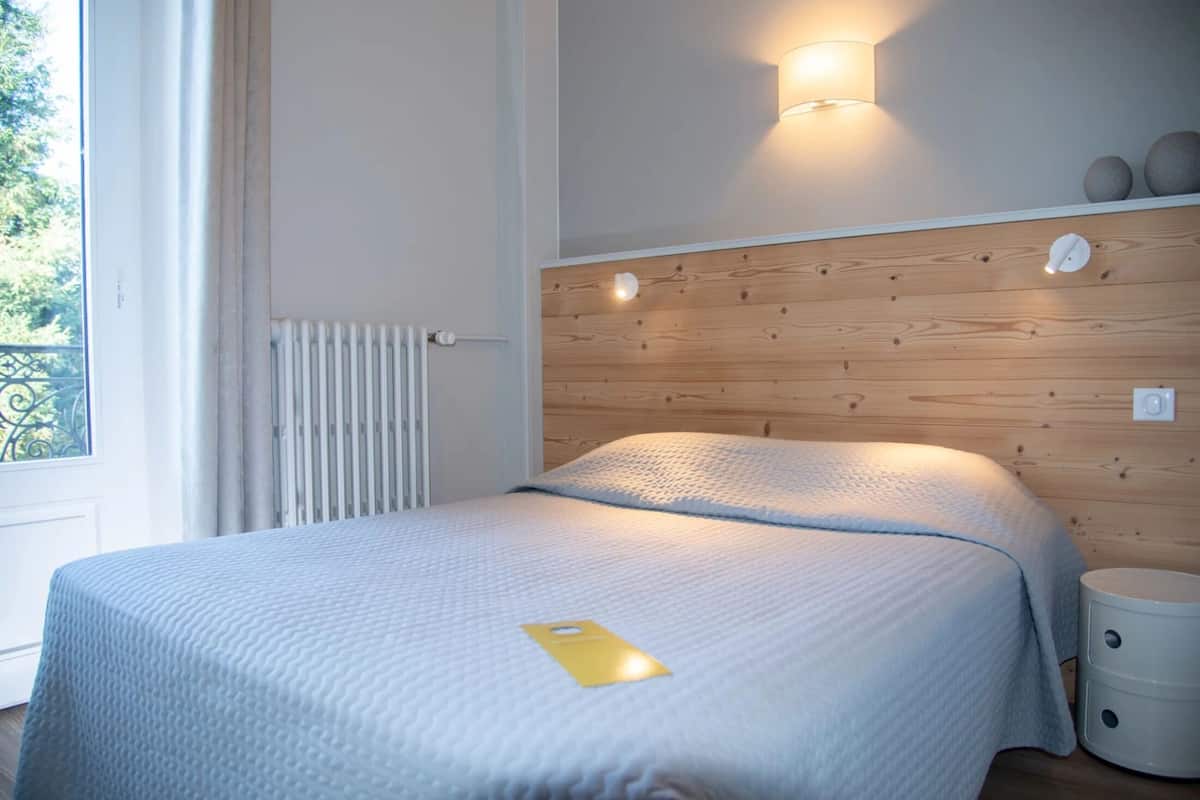 Un dormitorio con cabecera de madera, una mesita de noche y ventana con vistas a la vegetación.