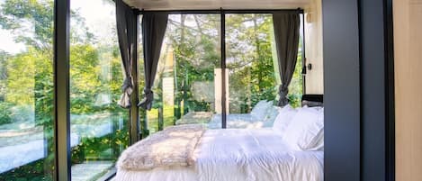 Een moderne slaapkamer met een groot bed, uitzicht op groen doorgaande ramen en een houten plafond.