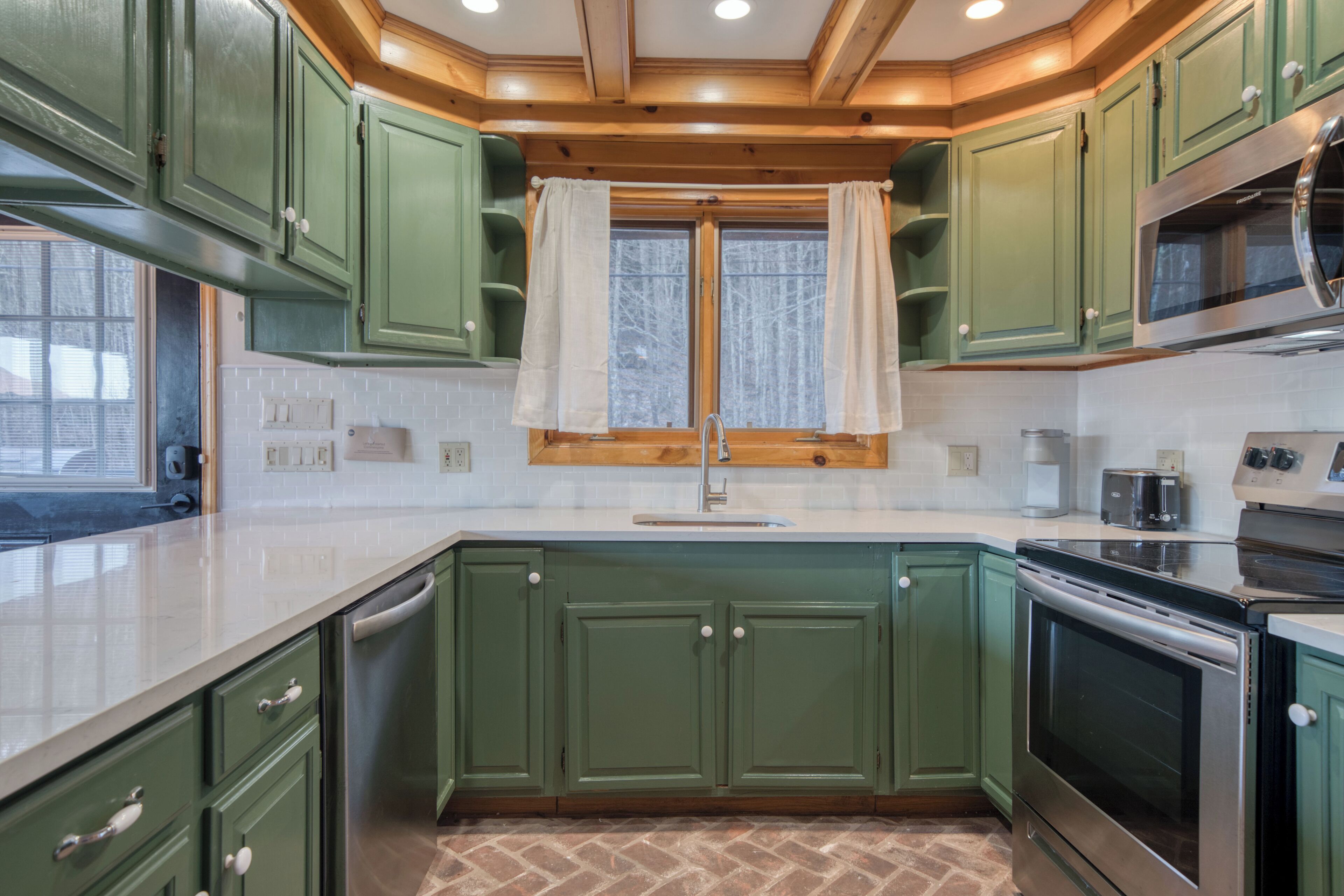 Una cocina con gabinetes verdes, un horno de acero inoxidable y un ventanal con cortinas.
