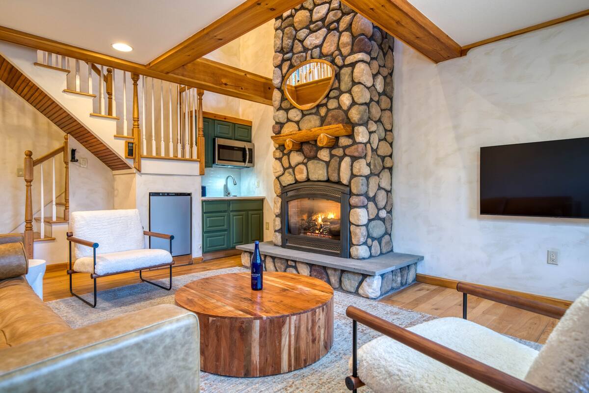 A spacious living room with a stone fireplace, wooden staircase, and modern furniture.