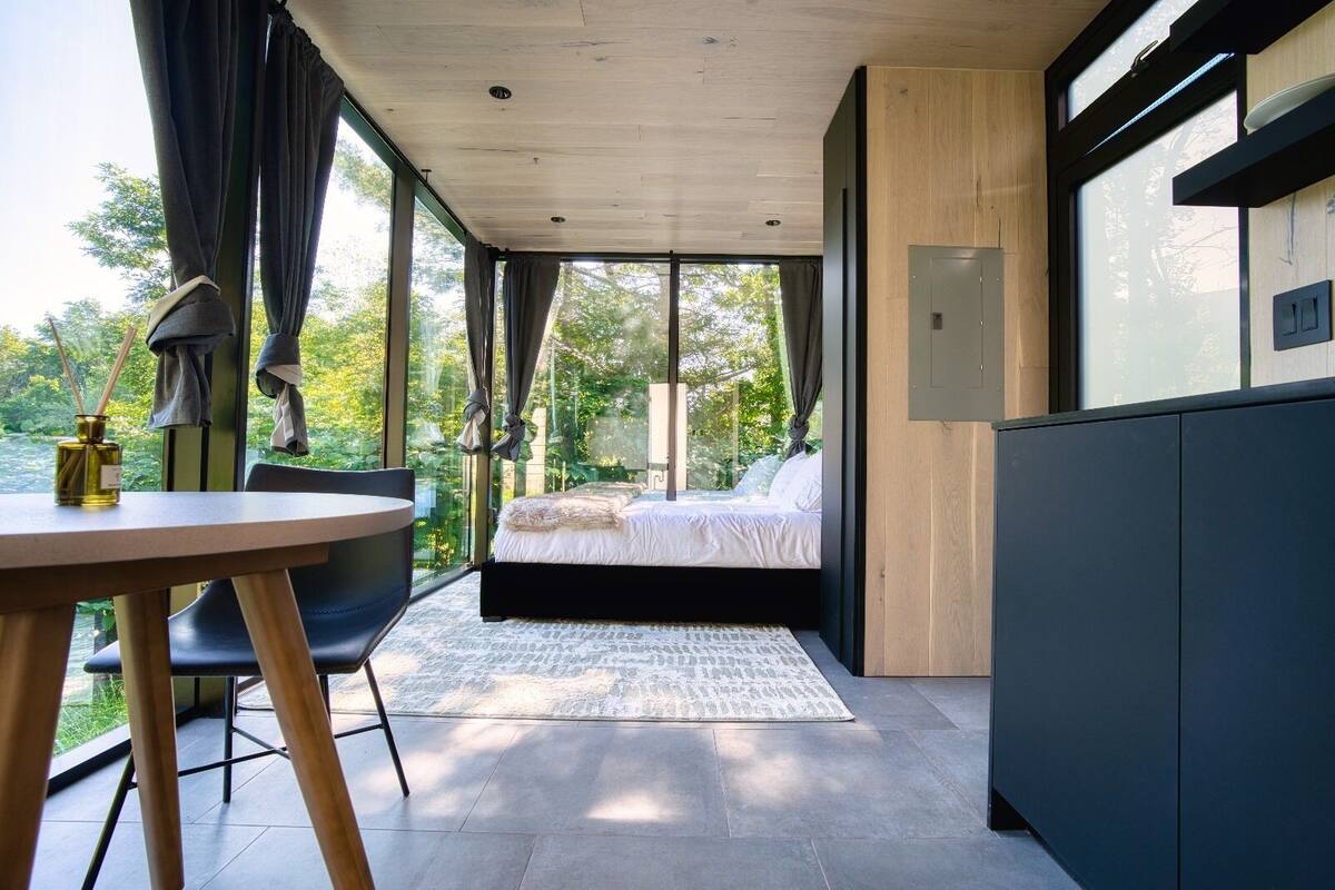 A modern bedroom with a large window, a bed, a table, and a chair.