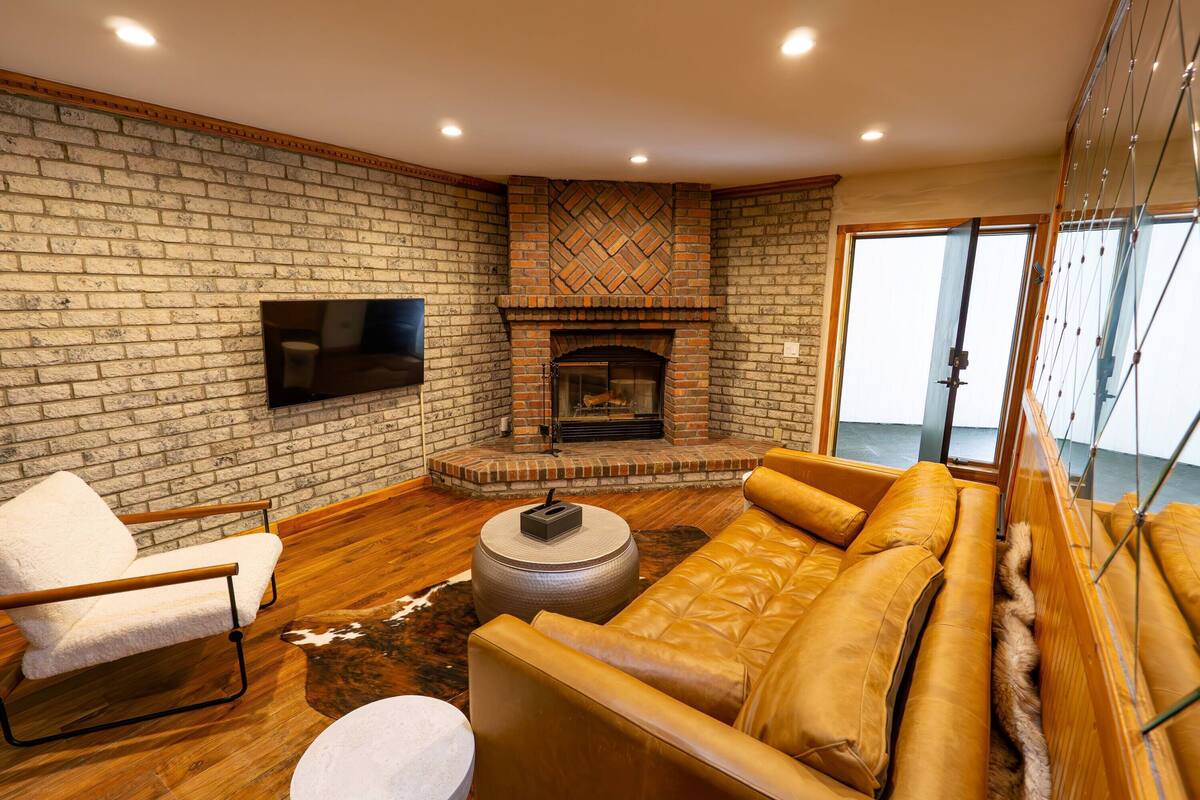 A living room with a brick wall, a fireplace, a sofa, a chair, and a television.