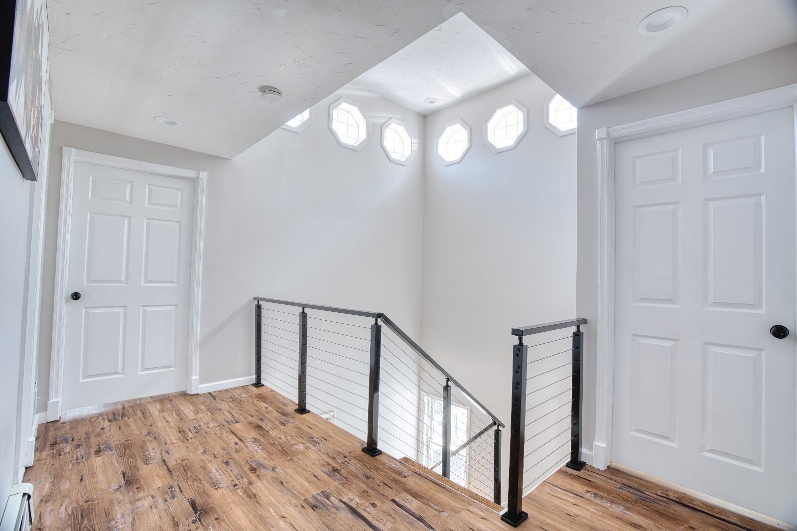 A staircase with wooden flooring and metal railings, leading to a room with white walls and doors.