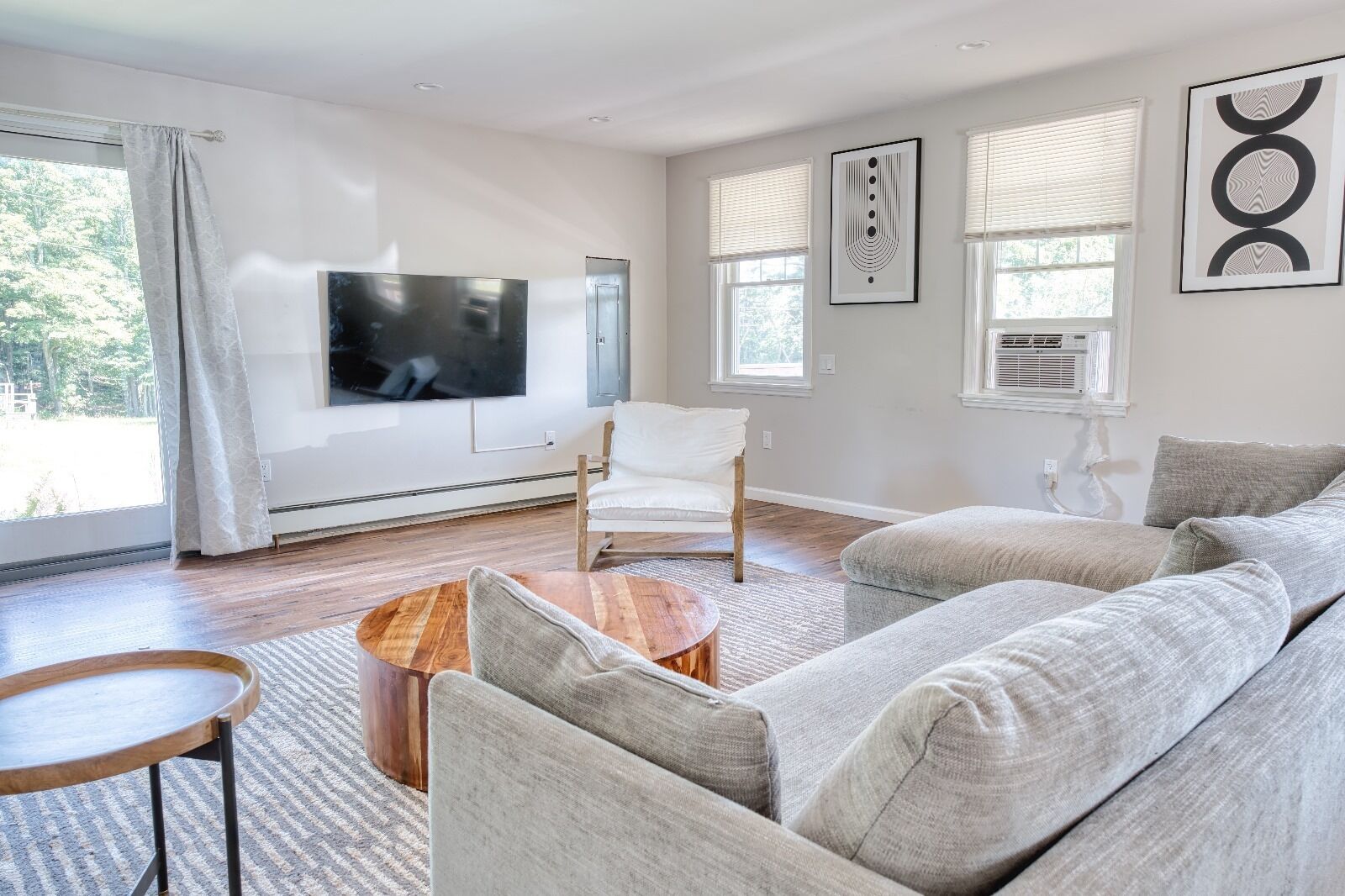A modern living room with a large flat-screen TV, a white armchair, a grey sofa, and a wooden coffee table.