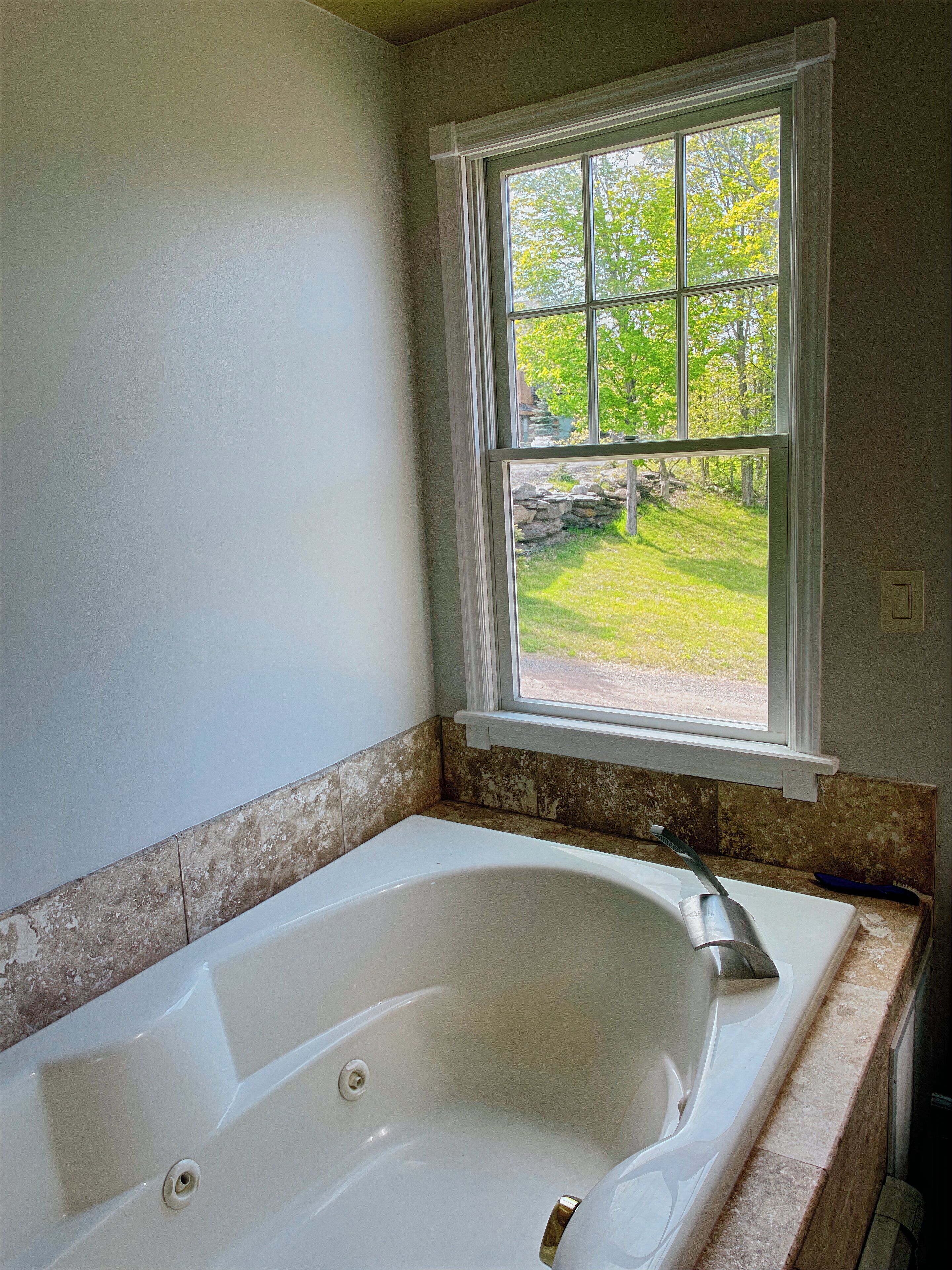 A bathroom with a large bathtub, a window with a view of a grassy yard, and a stone-tiled shower area.