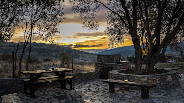 Un patio al aire libre con suelo de piedra, bancos de madera y una mesa lista para comer.