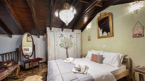 Un dormitorio con una cama grande, vigas de madera en el techo, un candelabro, un espejo y un cuadro de un árbol en la pared.