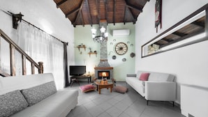 Una sala de estar con chimenea, sofás blancos, un televisor y una pared de piedra.