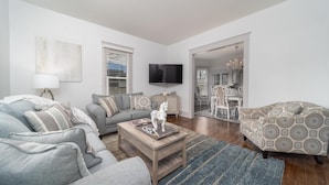 A spacious living room with a grey sofa, a patterned armchair, a wooden coffee table, and a TV mounted on the wall. - Great Location! 2 Houses for large groups!! (Grand Junction)