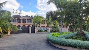 A gated entrance with a well-maintained garden, a large building with arched windows, and a clear sky. - Palmview Estate Townhouse (ocho rios)