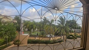 A view through a metal gate of a landscaped area with palm trees and a paved walkway. - Palmview Estate Townhouse (ocho rios)
