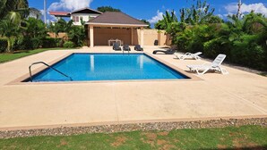 A rectangular swimming pool with a clear blue water, surrounded by a concrete deck. There are lounge chairs and a small table with chairs in the pool area. - Palmview Estate Townhouse (ocho rios)