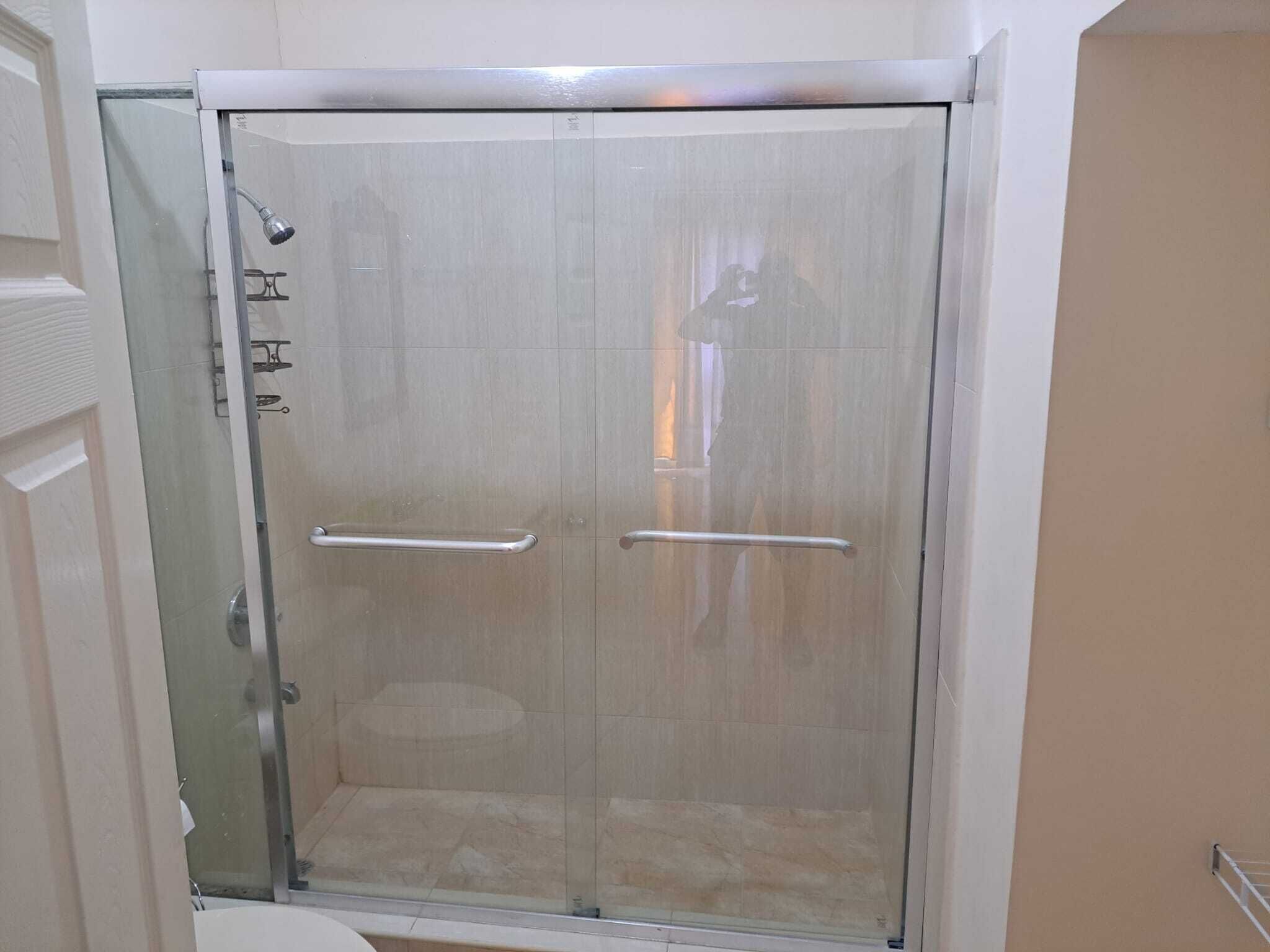 A glass-enclosed shower stall with a showerhead, a handrail, and a glass door.