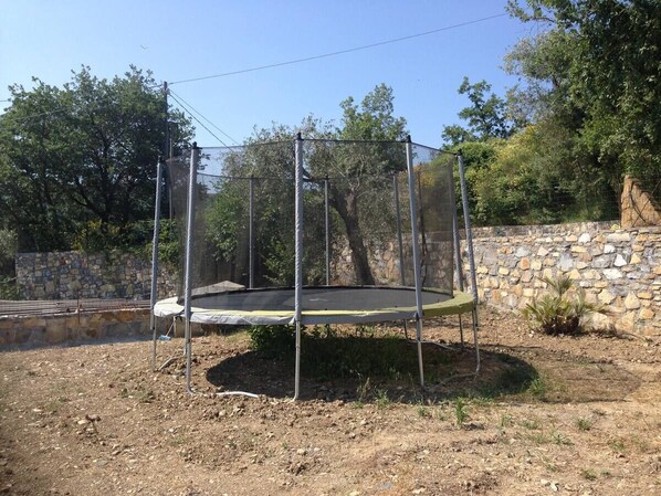 Un trampoline installé dans un espace extérieur, avec un mur de pierre et des arbres en arrière-plan.