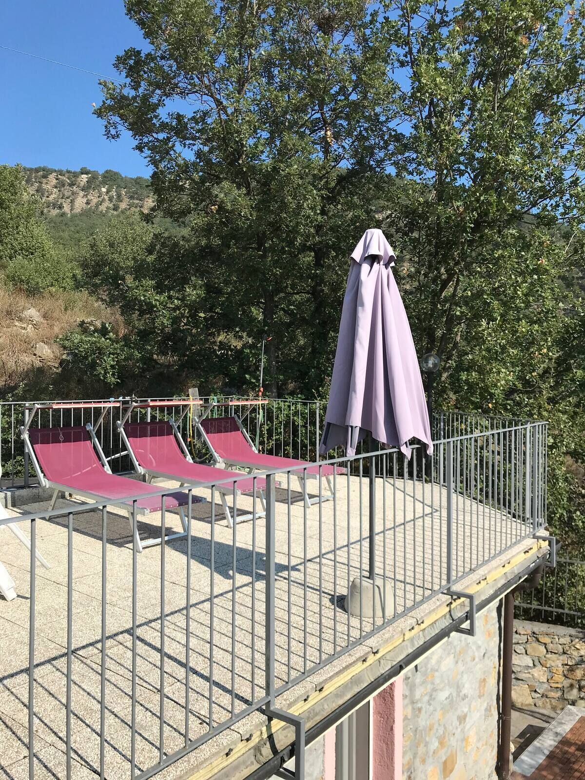 A rooftop terrace with two red lounge chairs and a purple umbrella.
