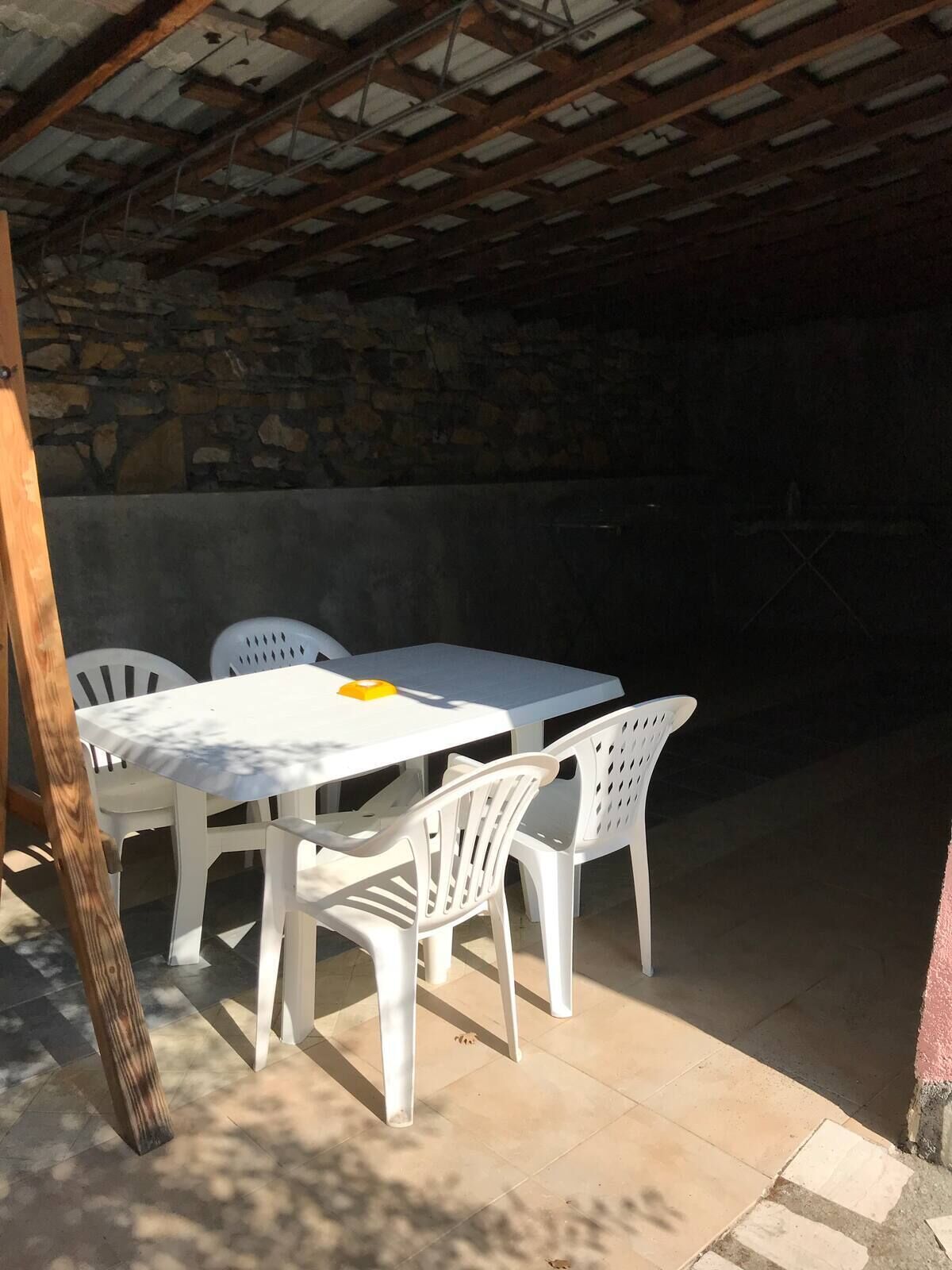 Un patio exterior con una mesa blanca y cuatro sillas de plástico blanco.