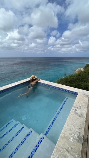 Una piscina con vista sull'oceano, una persona nella piscina e un ambiente tropicale.