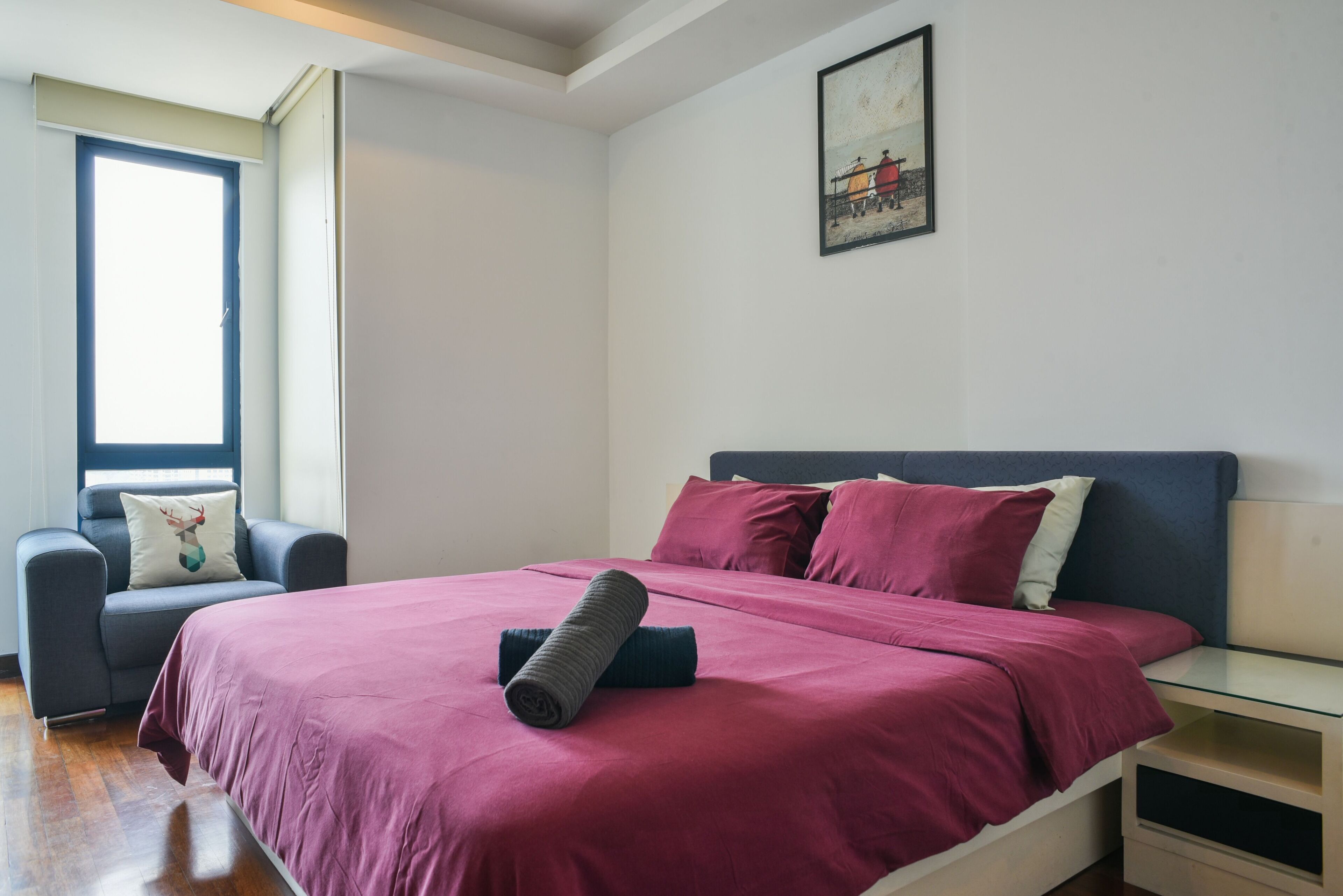A bedroom with a bed, a chair, a window, and a painting on the wall.